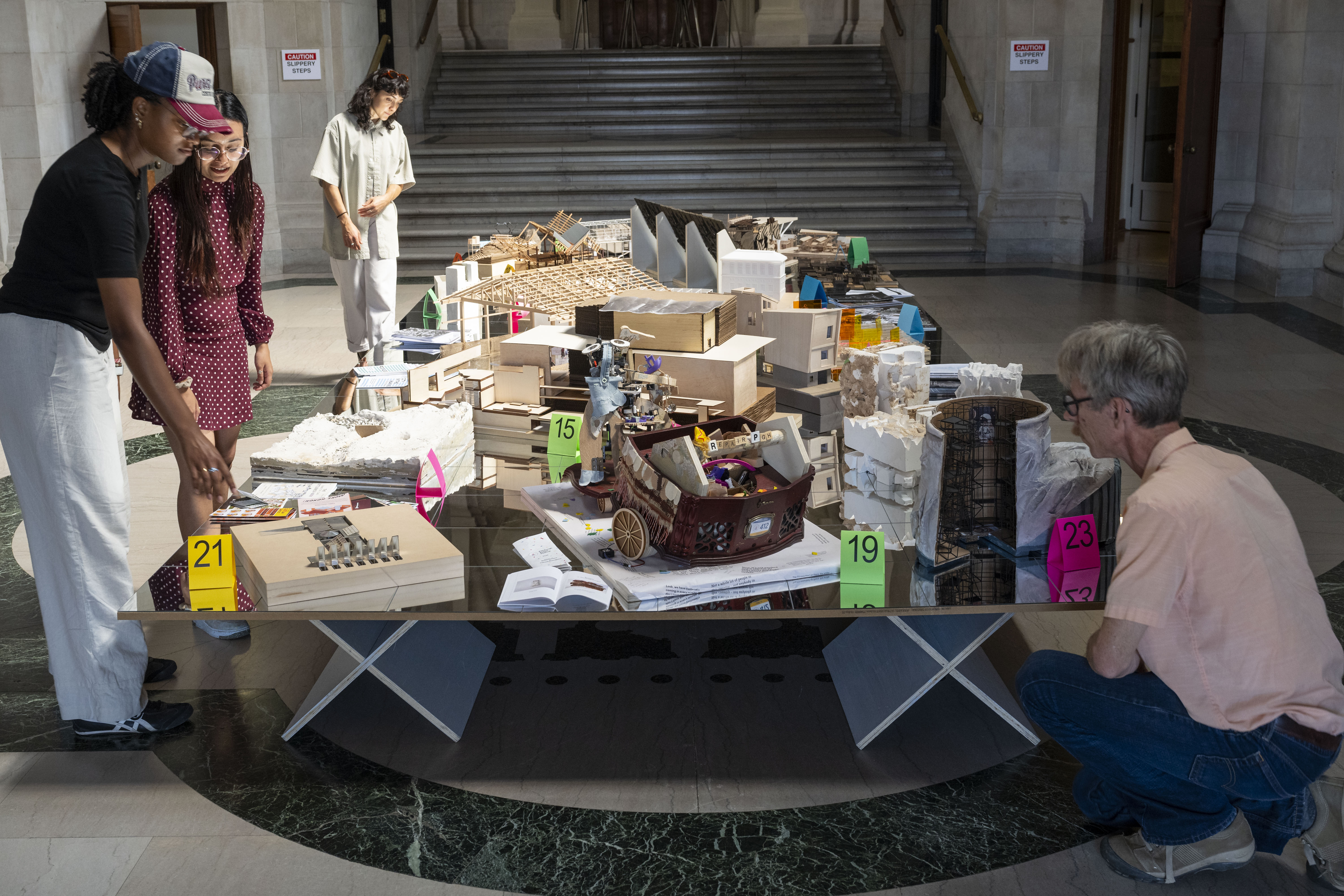 The exhibition's Table of Contents displays one representational model or object from each course in the exhibition. The mirrored surface of the table reflects the murals on the Great Hall ceiling.