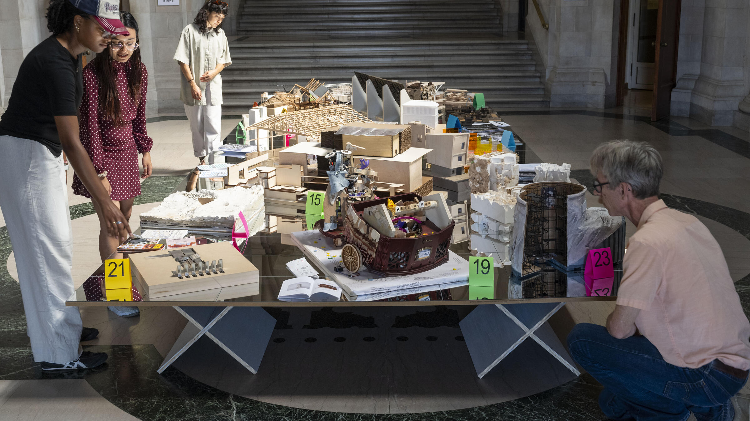 The exhibition's Table of Contents displays one representational model or object from each course in the exhibition. The mirrored surface of the table reflects the murals on the Great Hall ceiling.