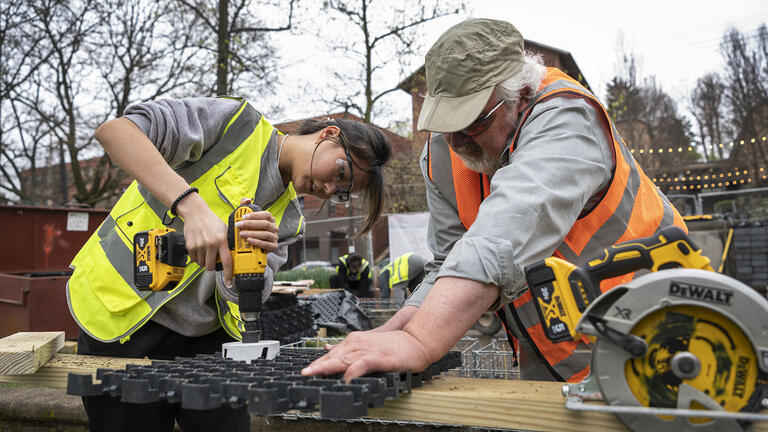 two people use power equipment to cut wood