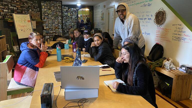 Group gathers around a table with a laptop