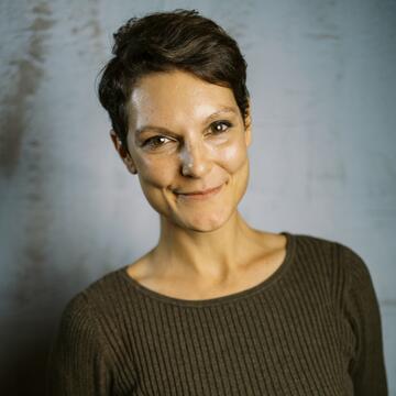 person with short hair wearing brown shirt on a neutral background