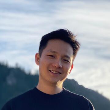 person with short hair and a black t-shirt with a mountain in the background