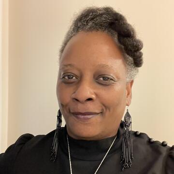 person with black top, long black earrings, silver necklace on a neutral background