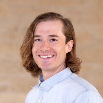 person with medium length hair wearing a blue button down shirt on a tan background