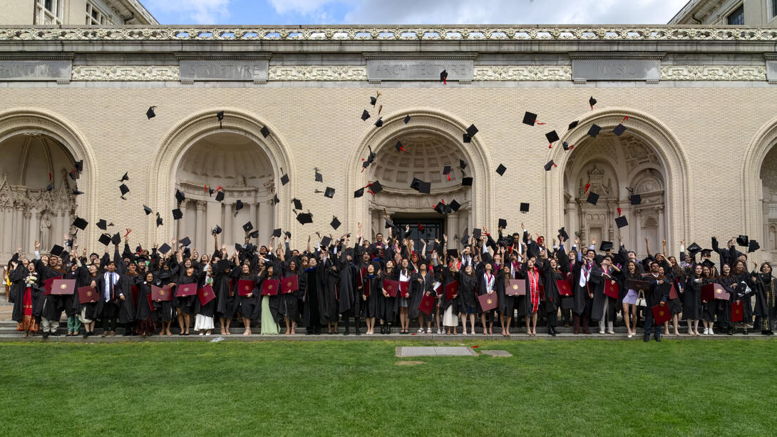 graduates throw their caps in front of the College of Fine Arts