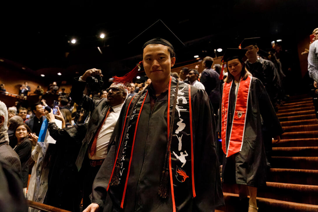 a student looks at the camera as they process into the theater for the graduation ceremony